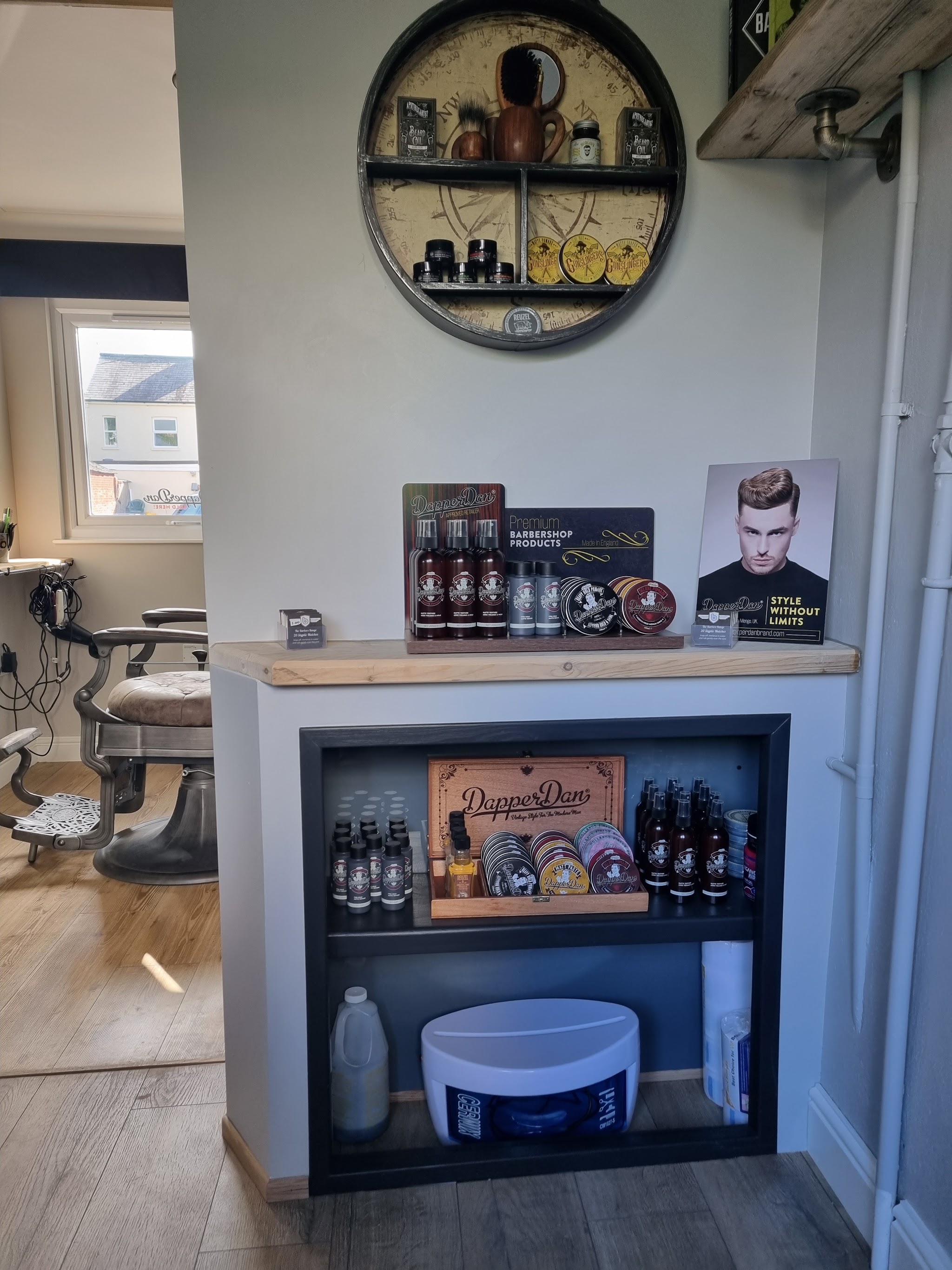 Shelf of barbershop products below the round wall shelf, with a vintage chair beyond